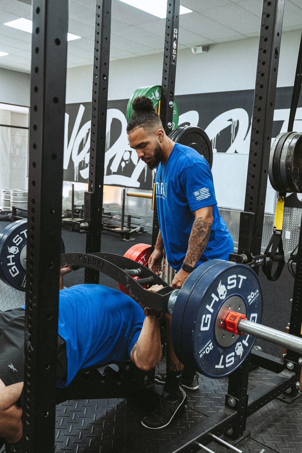 Man spotting another man bench pressing heavy weights at the gym.